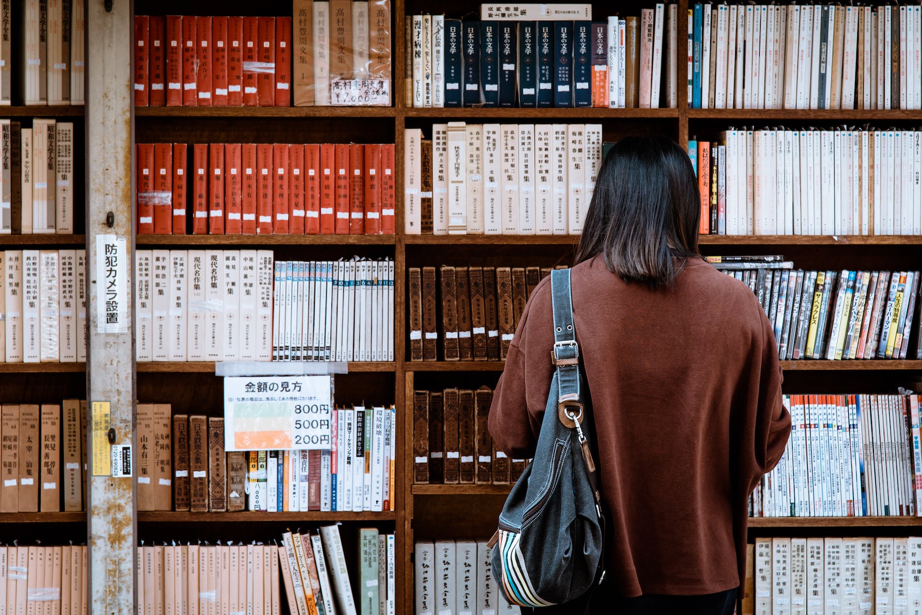 woman wearing brown shirt carrying black leather bag on front of library books conducting research